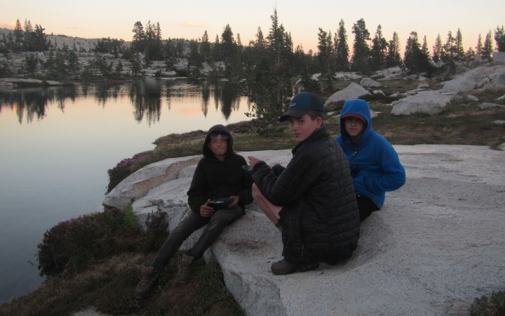 three outward bound students rest on a rock beside an alpine lake